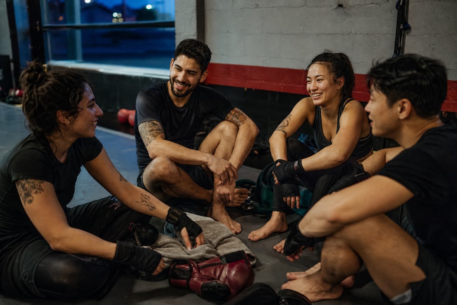 Four fictional adult athletes relax together after a controlled technical sparring session.
